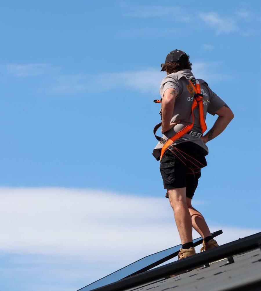 Element Power Co installer standing on a roof ridge in a safety harness, checking a new solar array